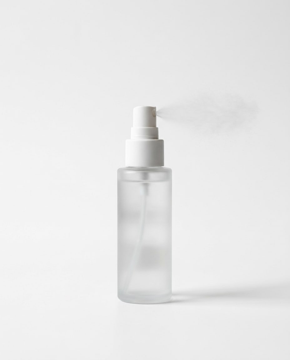 Setting Veil: a frosted-glass spray bottle, a fine cloud of mist just leaving the nozzle.